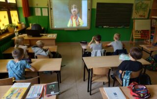 Klasa szkolna. Uczniowie siedzą w ławkach i oglądają bajkę pod tytułem "Jak zostałem bohaterem".