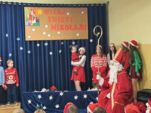 Święty Mikołaj w towarzystwie pięciu uczennic i jednego dziecka przedszkolnego na sali gimnastycznej