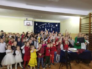 Społeczność szkolna znajduje się na sali gimnazstycznej szkoły i bierze udział we wspólnym śpiewaniu kolęd ze szkołami partnerskimi z Brzozowej i Berlina
