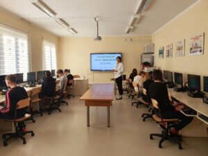 Ośmioro uczniów klasy VIII rozwiązuje test przy komputerze podczas konkursu "Prawa i obowiązki uczniów". Po środku sali stoi nauczycielka organizująca konkurs.