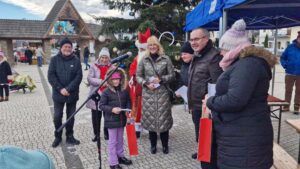 Uczennica klasy I Szkoły Podstswowej w Kadczy odbiera nagrodę. Na zdjęciu znajduje się Święty Mikołaj i sześć osób, które są organizatorami konkursu.