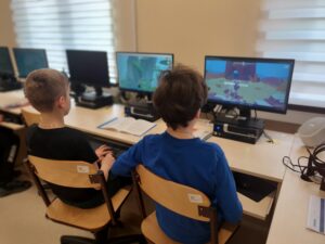 Dwóch uczniów klasy 5 siedzi przy komputerach w sali komputerowej i bierze udział w grze Asy intenernetu