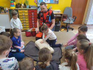 Ratownik medyczny i dziesięcioro przedszkolaków podczas ćwiczeń z udzielania pierwszej pomocy