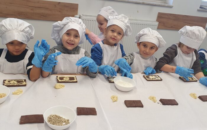 grupa dzieci w czapkach kucharskich, fartuchach i rękawicach wykonujące słodycze