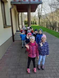 Dzieci z oddziału przedszkolnego idą na spacer. W tle budynek szkoły.