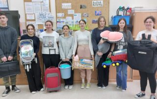 Uczniowie klasy 8 z nosidłami: etui na laptopa, wózek dla lalek, torba i waliza podróżna, wiaderko, łóżeczko dla lalki, pluszak, samochodzik