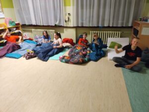 Uczniowie klasy piątej siedzą w sali lekcyjnej i rozmawiają. Przygotowują się do snu.