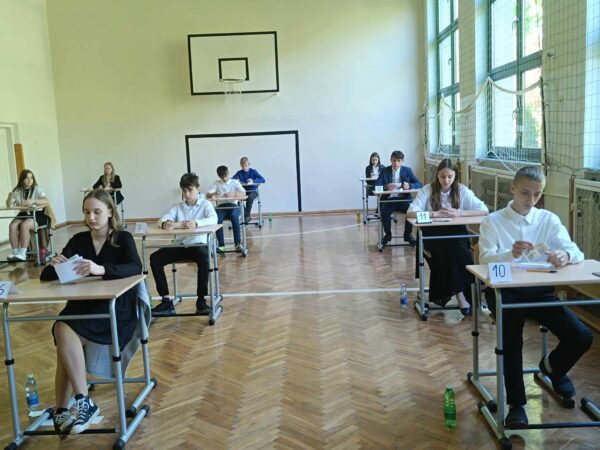 Uczniowie klasy ósmej oczekują w sali gimnastycznej na rozpoczęcie egzaminu.