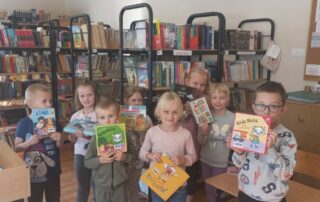 Dzieci w bibliotece szkolnej prezentują, wybrane przez siebie do pożyczenia, książeczki.