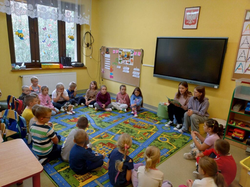 Uczennice starszych klas czytają głośno swoim młodszym koleżankom i kolegom.