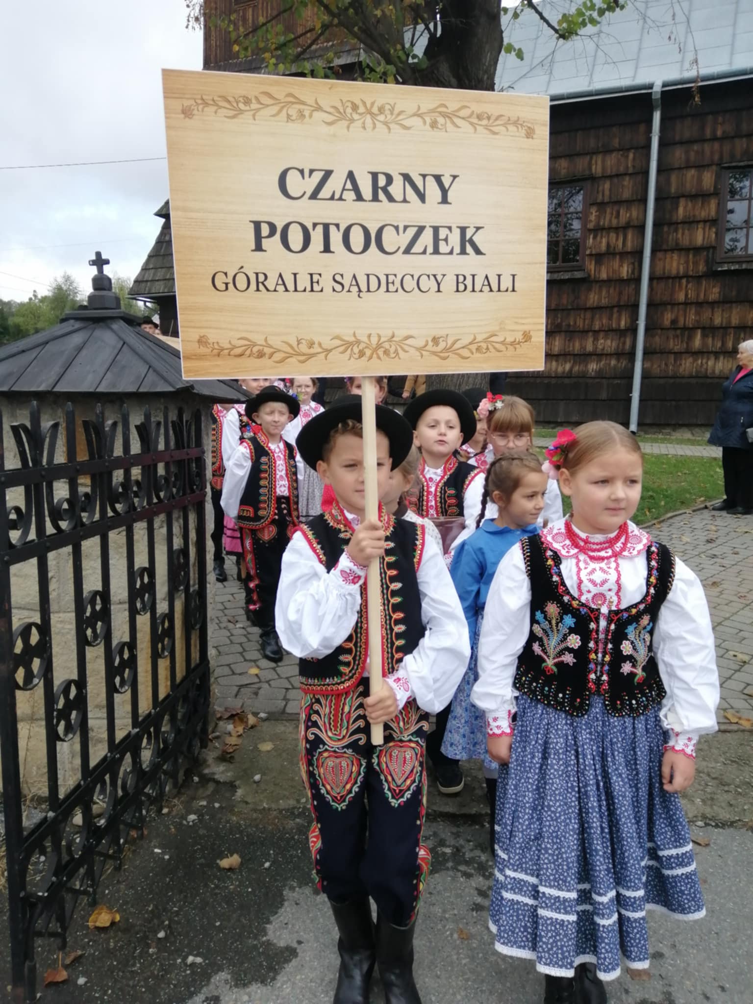 Przemarsz w korowodzie z kościoła na parking. Członkowie Zespołu niosą transparent Czarny Potoczek górale sądeccy biali