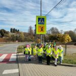 Uczniowie w kamizelkach odblaskowych pod znakiem drogowym