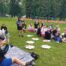 Uczniowie na zielonym placu, siedzą na kocach lub karimatach i pokazują ulubione książki