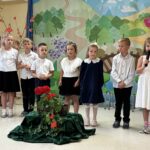 Dzieci ubrane na galowo (strój bialo-czarny/granatowy) recytują wiersz. W tle płótno dekoracyjne - krajobraz letni.