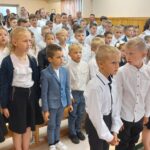 Uczniowie w strojach galowych stoją na baczność podczas śpiewania Hymnu