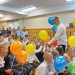 Dwóch uczniów klasy 8 wręcz pierwszoklasistom kolorowe baloniki na patyku