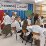 Uczniowie w scenerii opisanej przy pierwszym zdjęciu czytają utwory Jana Kochanowskiego. Dodatkowo 6 dziewczynek ubranych w kolorowe zwykle kwieciste sukienki i z wiankami na głowach tańczą w kółeczku.
