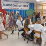 Uczniowie w scenerii opisanej przy pierwszym zdjęciu czytają utwory Jana Kochanowskiego. Dodatkowo 6 dziewczynek ubranych w kolorowe zwykle kwieciste sukienki i z wiankami na głowach tańczą w kółeczku.