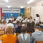 Uczniowie w scenerii opisanej przy pierwszym zdjęciu czytają utwory Jana Kochanowskiego - teraz utwór czyta jedenasty chłopiec. Widać też publiczność i panią organizatorkę.