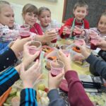 Uczniowie klasy drugiej naokoło stołu z kubeczkami z sokiem w rękach