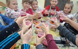Uczniowie klasy drugiej naokoło stołu z kubeczkami z sokiem w rękach