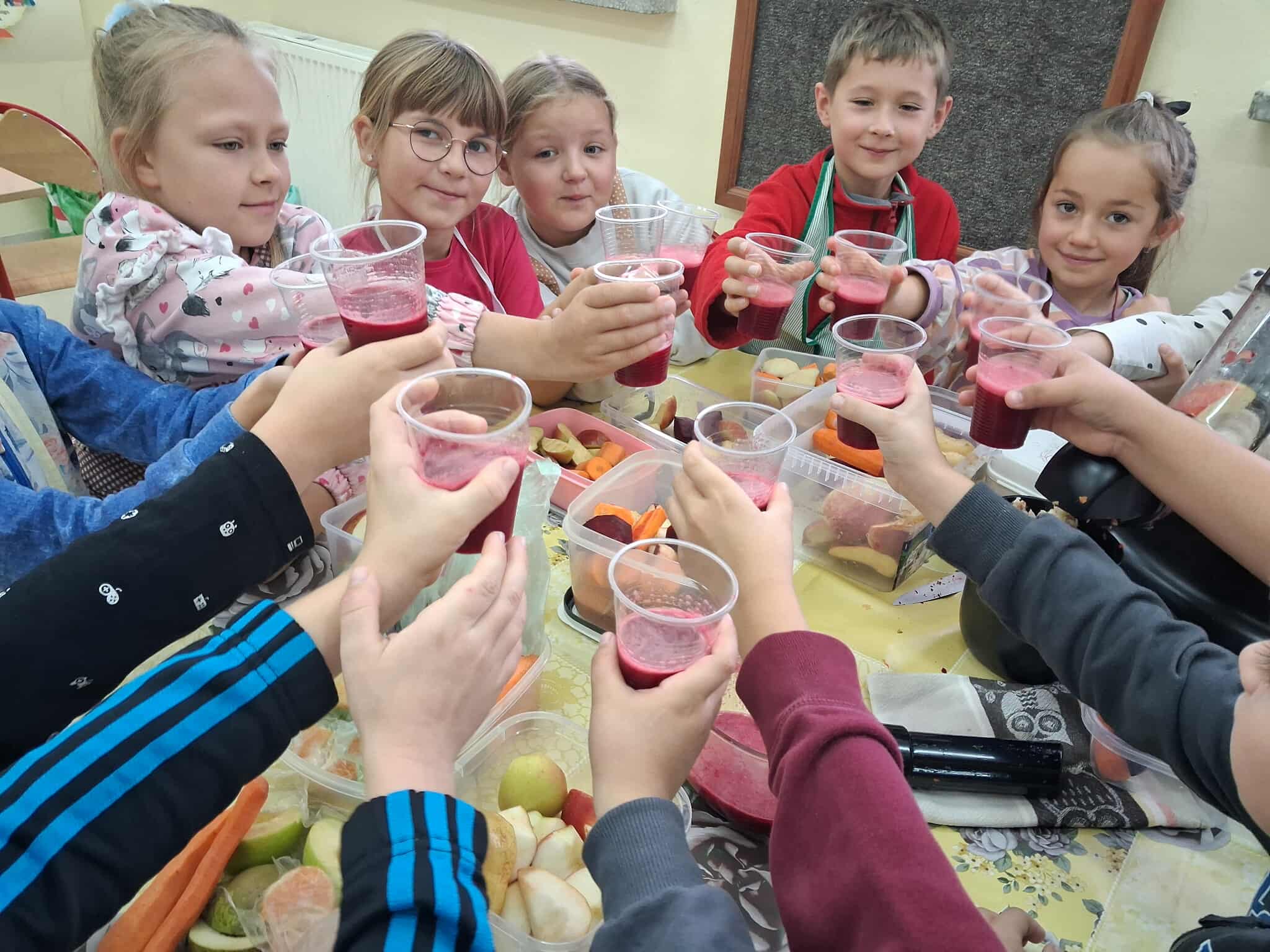 Uczniowie klasy drugiej naokoło stołu z kubeczkami z sokiem w rękach