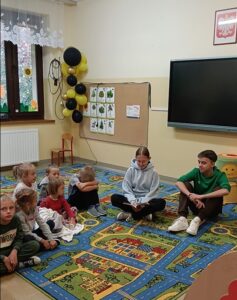 Uczniowie klasy 8 głośno czytają dzieciom w oddziale przedszkolnym.