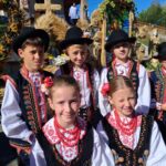 Zdjęcie zbiorowe uczniów - czterech chłopców i 2 dziewczynek w strojach regionalnych. W tle wieńce dożynkowe