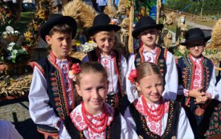 Zdjęcie zbiorowe uczniów - czterech chłopców i 2 dziewczynek w strojach regionalnych. W tle wieńce dożynkowe