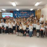 Przedszkolacy i uczniowie w strojach odświętnych śpiewaja hymn