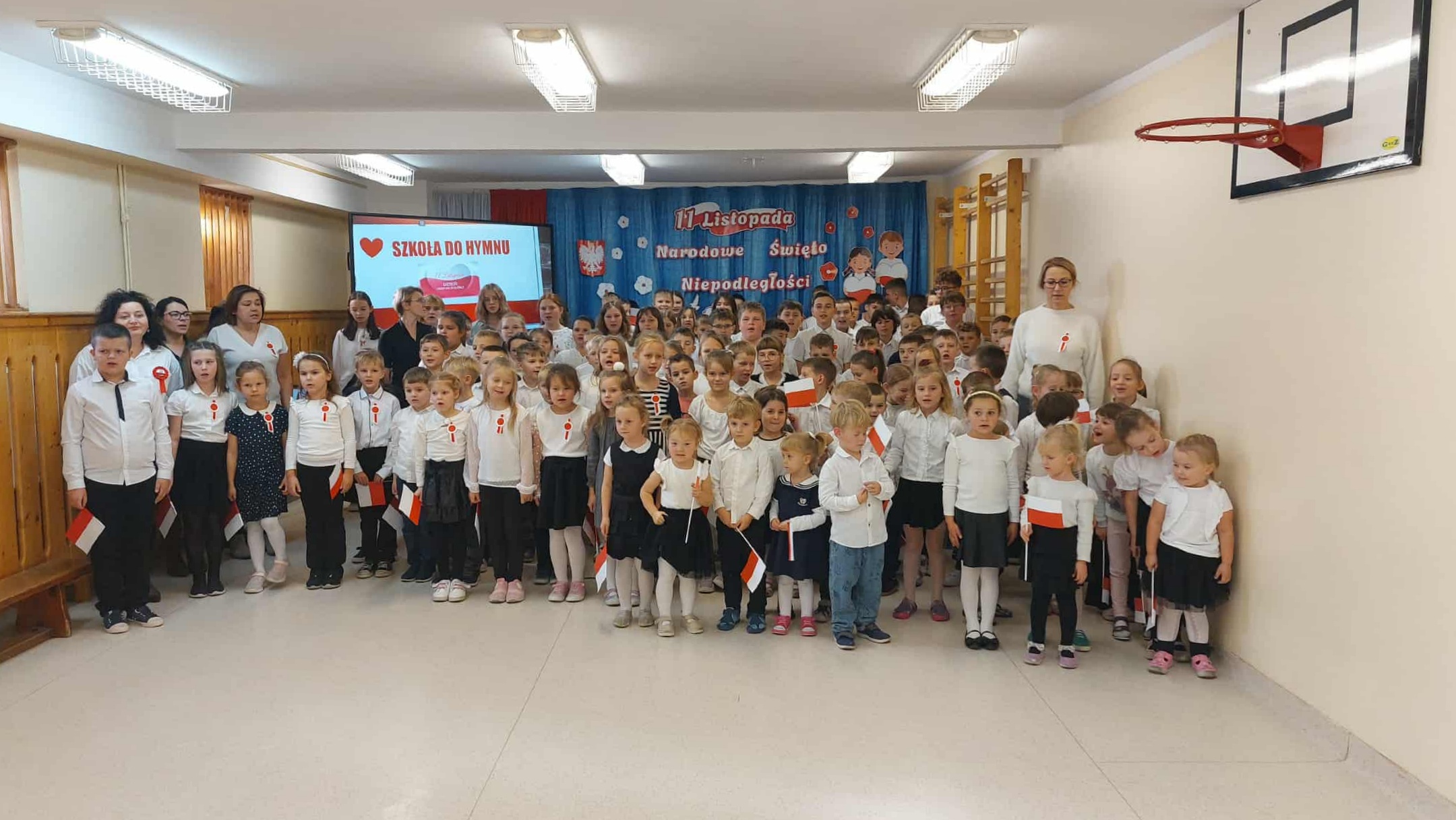 Przedszkolacy i uczniowie w strojach odświętnych śpiewaja hymn
