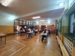 Uczniowie klasy 8 podczas pisania próbnego egzaminu w sali gimnastycznej
