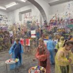 Uczniowie w Pokoju Ekspresji - ubrani w peleryny, na ścianach rozwieszona płótna na obrazy, które uczniowie malują, ściany pochlapane i pomalowane farbami