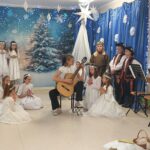 Dziewczynka gra na gitarze, wokół klęczą lub kucają aniołki
