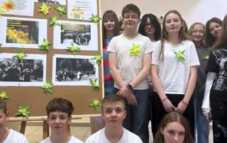 Uczniowie kl. 7 i 8 obok wystawki z żonkilami zrobionymi z papieru przypiętymi do białych podkoszulek