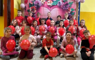 Na zdjęciach widać dzieci z czerwonymi balonami w kształcie serca na tle kwiecistego płutna.