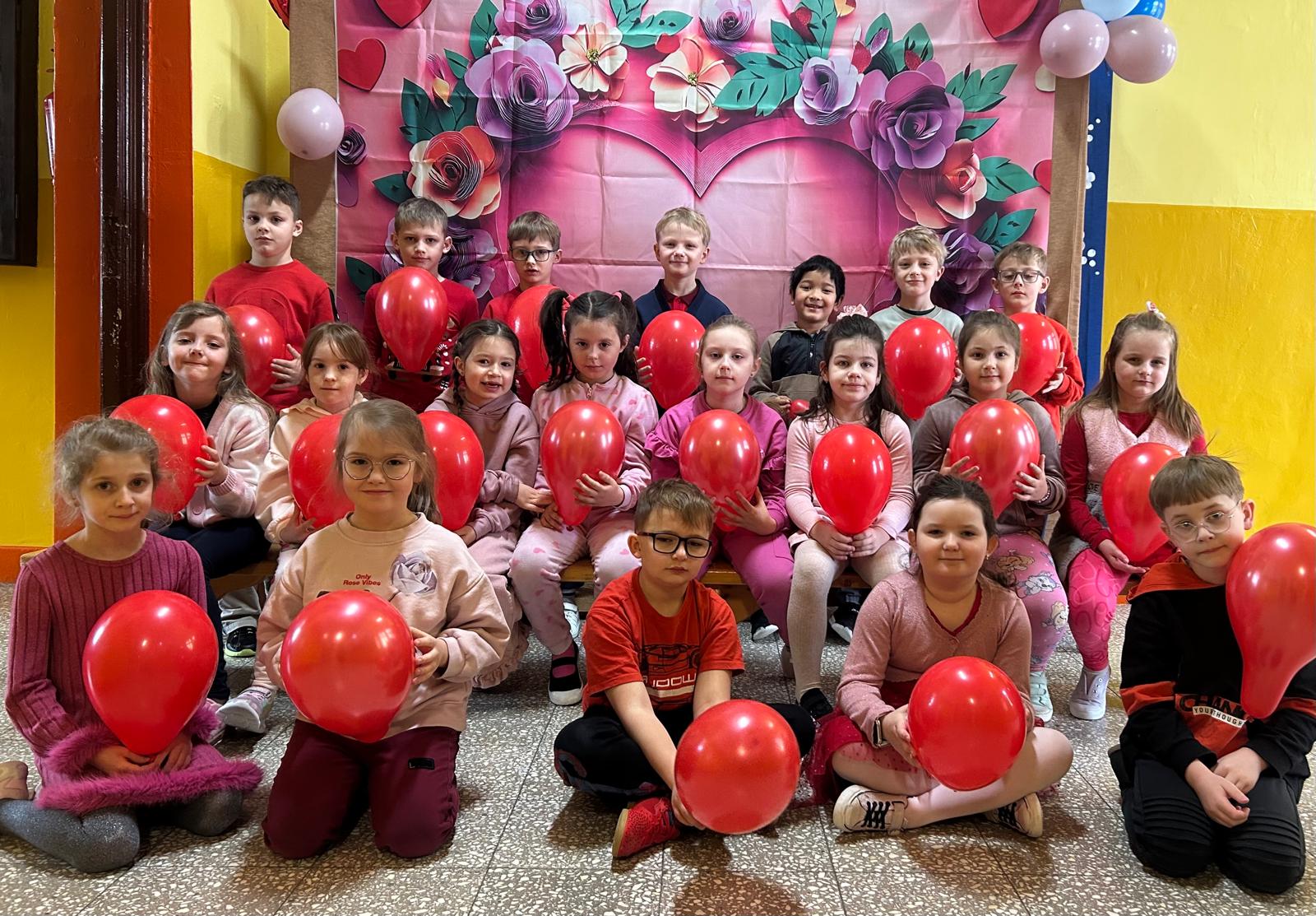 Na zdjęciach widać dzieci z czerwonymi balonami w kształcie serca na tle kwiecistego płutna.