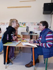 Na zdjęciach widać dzieci słuchające z zaciekawieniem autorki książeczek dla dzieci, któa opowiada o pracy pisarza. Dzieci trzymają książeczki z dedykacją od samej autorki.