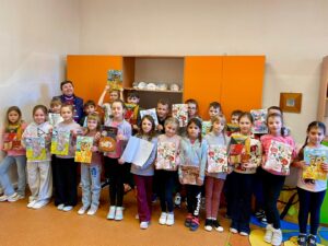 Na zdjęciach widać dzieci słuchające z zaciekawieniem autorki książeczek dla dzieci, któa opowiada o pracy pisarza. Dzieci trzymają książeczki z dedykacją od samej autorki.